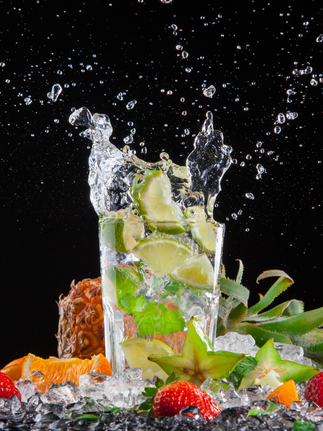 A close up of a splashing drink in a glass. The drink is a mojito, and it is made with white rum, mint leaves, lime juice, and sugar. The image is used to promote mojitos, and to highlight the refreshing and delicious flavors of this cocktail.