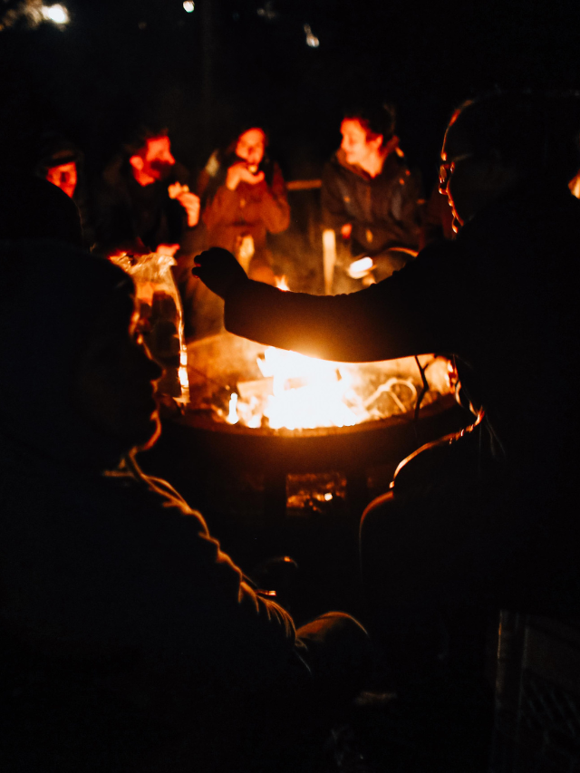 A group of people sitting around a campfire at night on Mandarmani Beach in West Bengal, India. The image is relevant to the topic of how to organize a bonfire at Mandarmani Beach.